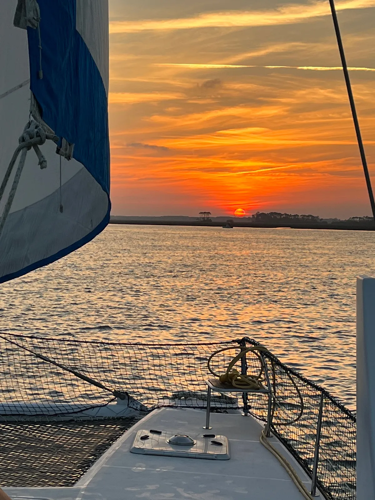The orange glow of sunset over the bow of the sailing catamaran