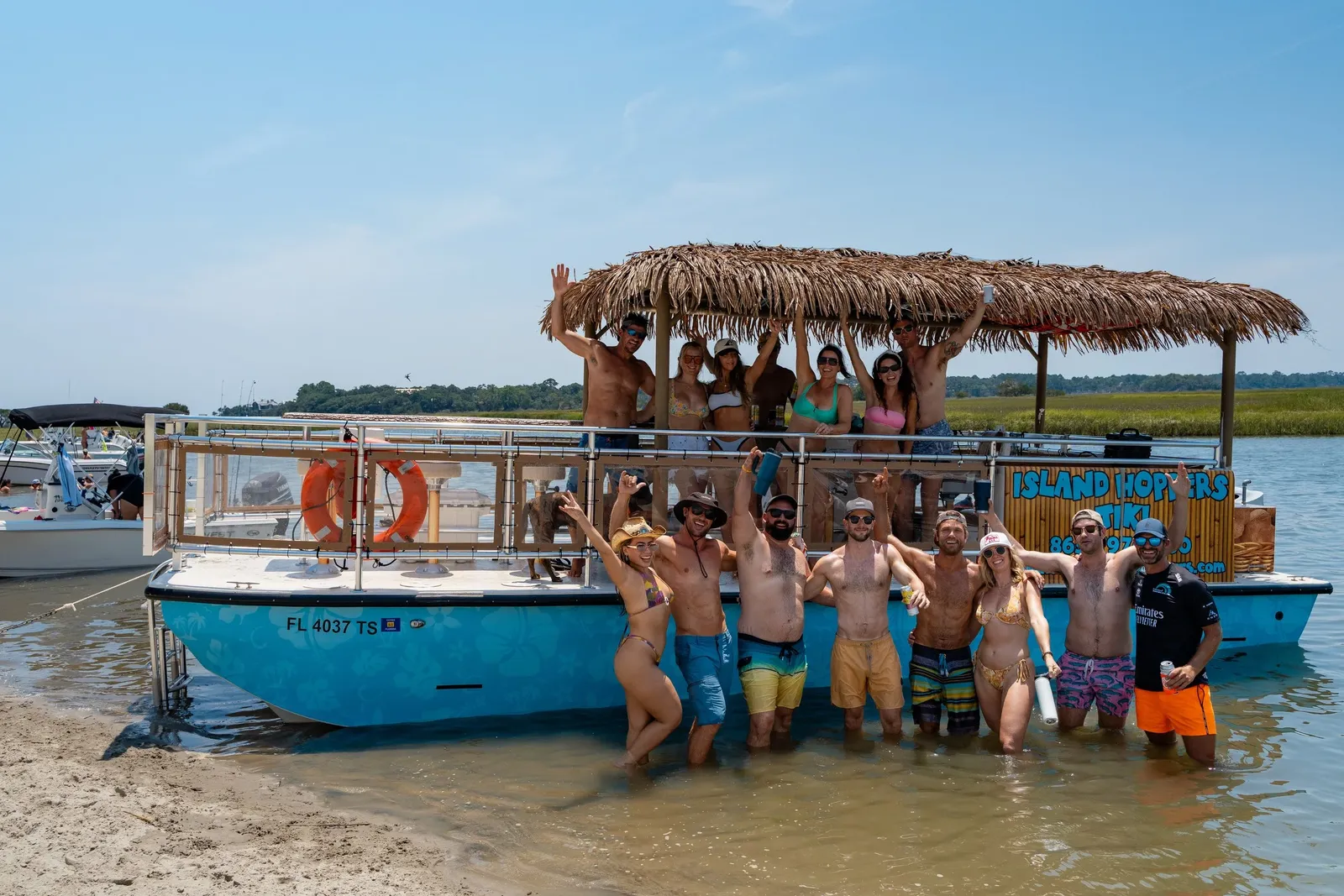 Tour group standing in the shallows beside the tiki boat at a sandbar near Folly Beach